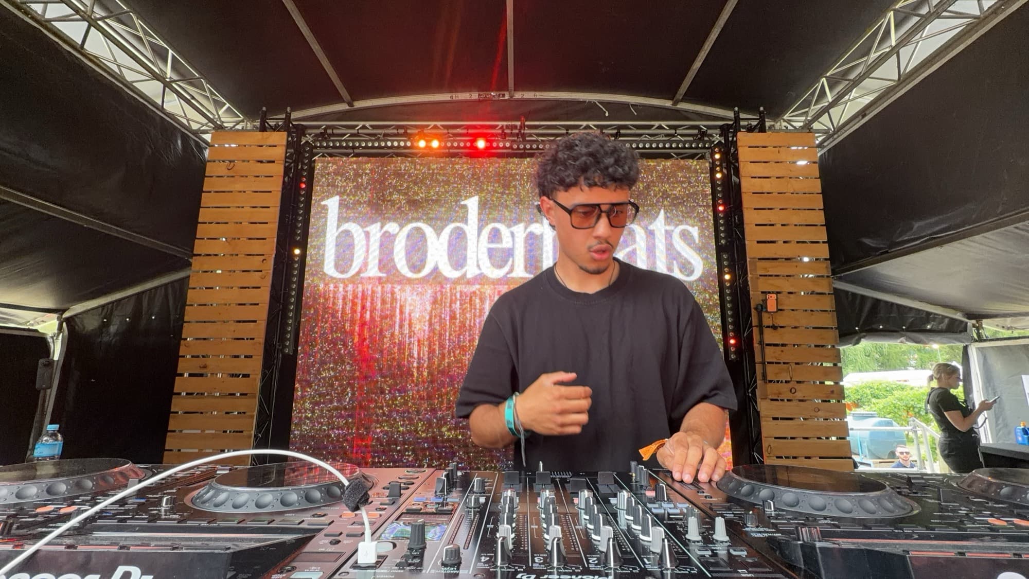 A DJ at the mixer, framed by timber panels and an LED screen