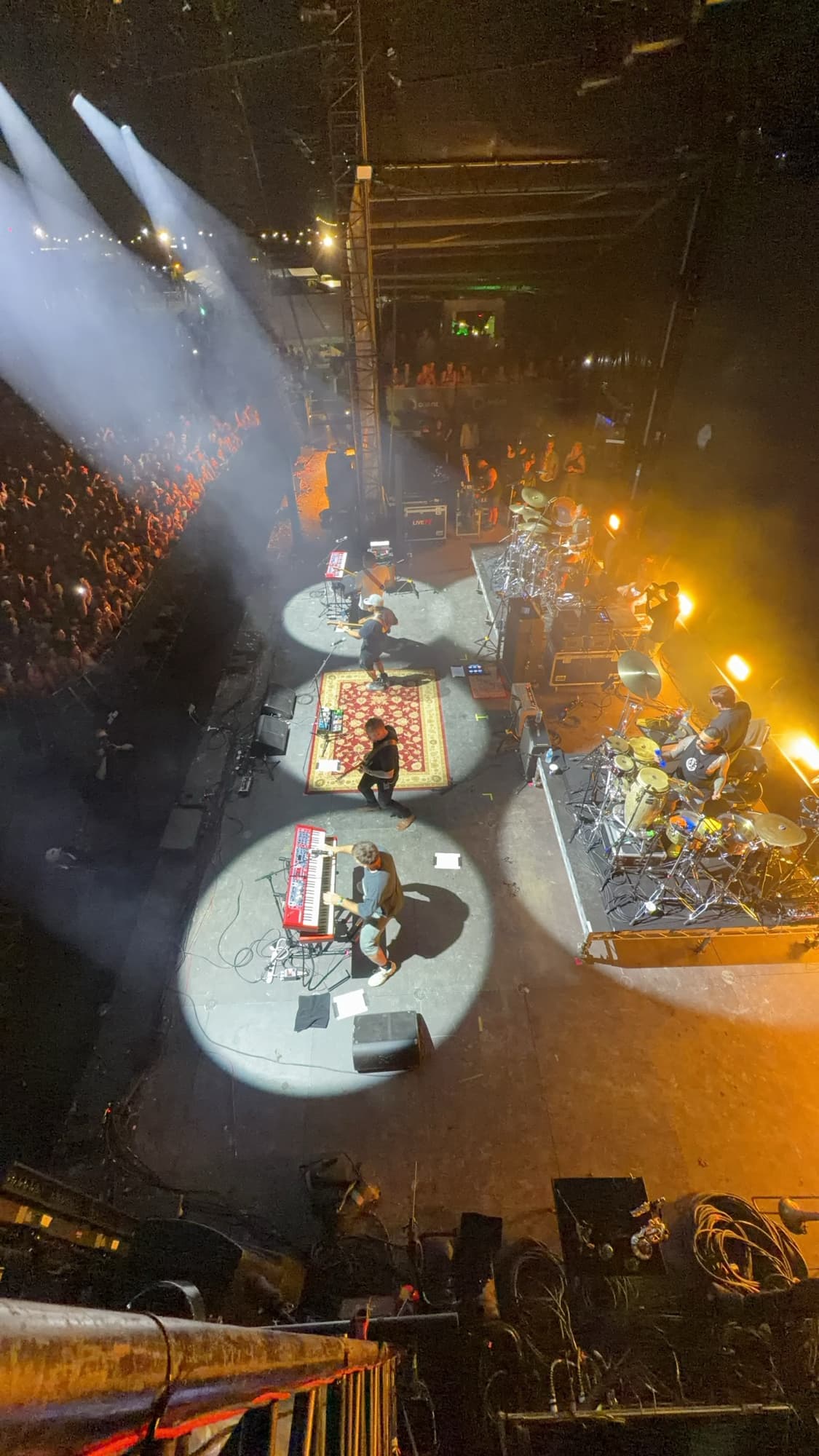 Looking down from the rig onto a drum riser lit by spotlights